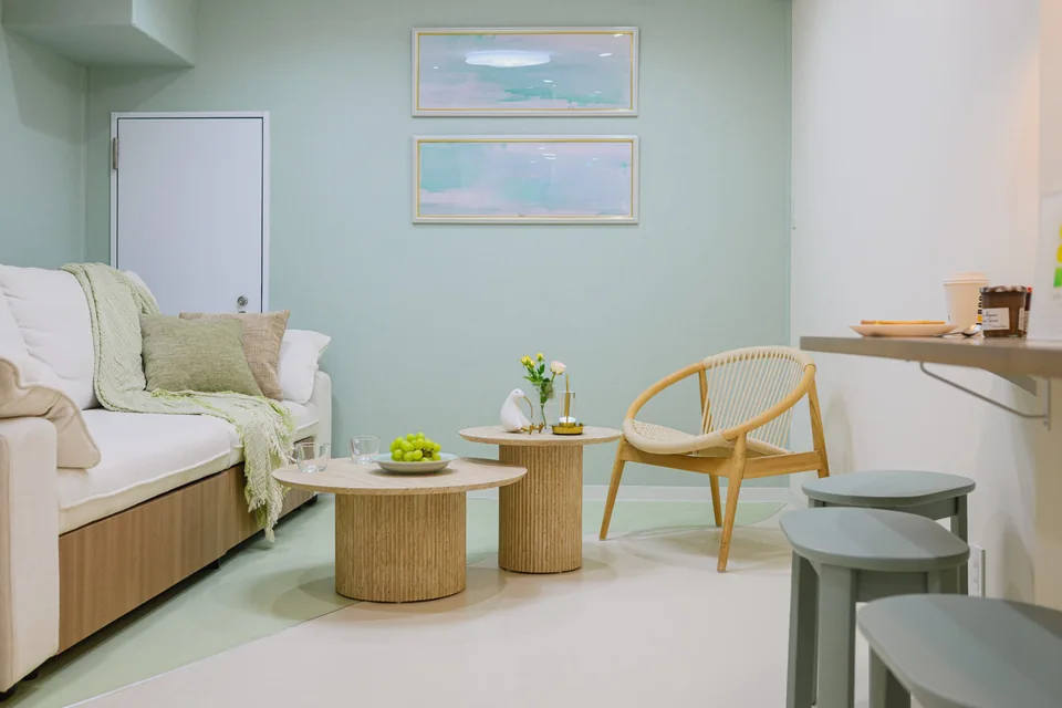 Mint-green walls, a white sofa and a round wooden table at ARiA STAY HATSUDAI.