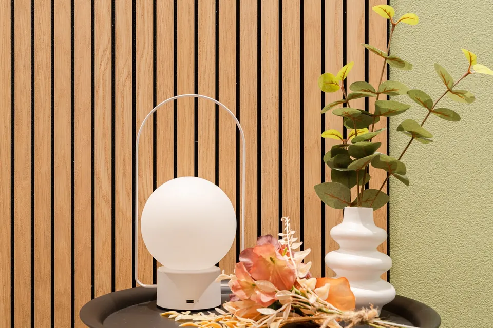 A round white lamp and wavy vase beside wooden slats and an olive wall at ARiA STAY SHINAGAWA.