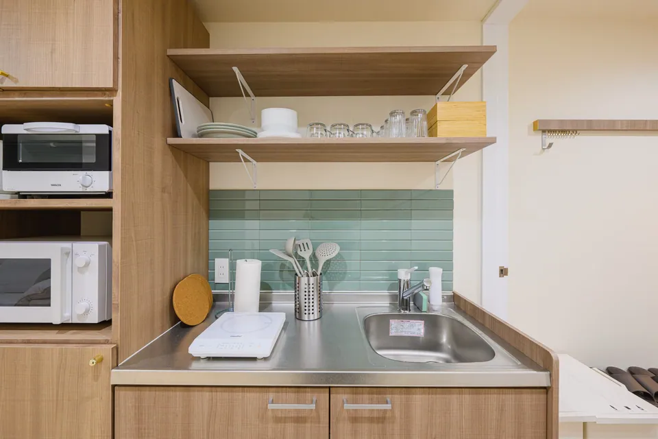 The kitchen with mint tiles and wooden shelves at ARiA STAY HATSUDAI