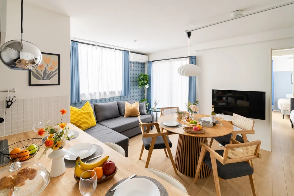 SB01: Blue & yellow. Blue patterned walls, yellow cushions and a round wooden dining table, with two bedrooms for families or friends.